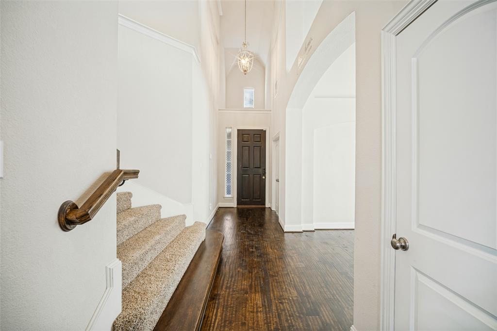 Foyer featuring vaulted ceilings, dark wood-finish flooring, a decorative pendant light fixture, carpeted staircase with a wood handrail, and an arched entryway Foyer featuring vaulted ceilings, dark wood-finish flooring, a decorative pendant light fixture, carpeted staircase with a wood handrail, and an arched entryway