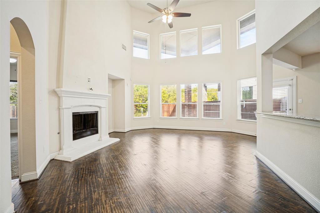 Two-story living area featuring wood-finish flooring, soaring ceilings, a white fireplace mantel, multiple window tiers, and a ceiling fan