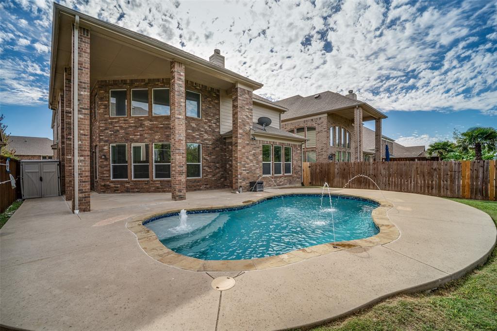 Brick exterior featuring a covered patio, free-form pool with water features, and concrete decking