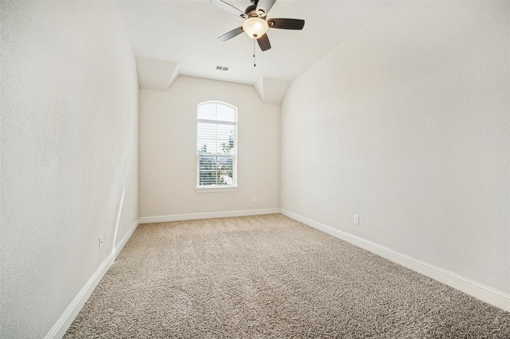 Room featuring neutral wall-to-wall carpeting, vaulted ceiling, arched window, and a multi-blade ceiling fan with integrated lighting