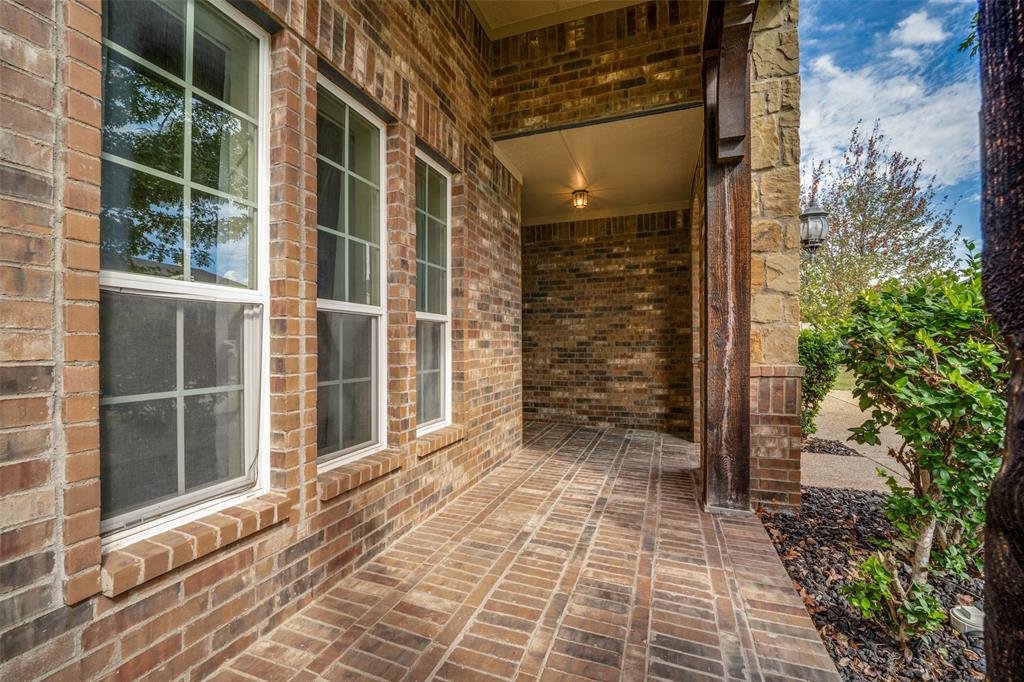 Covered entryway featuring brick masonry construction, grid-patterned windows, herringbone-laid brick flooring, and a stone-clad column Covered entryway featuring brick masonry construction, grid-patterned windows, herringbone-laid brick flooring, and a stone-clad column