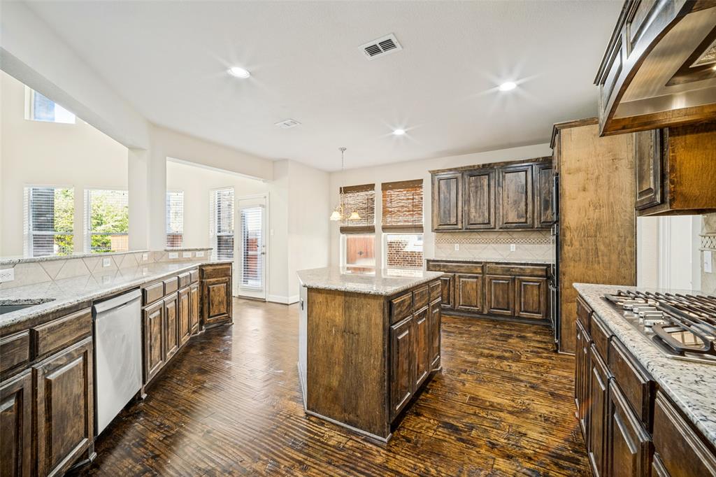 Kitchen featuring custom stained wood cabinetry, stone-surface countertops, central island, wood-finish flooring, and built-in stainless steel gas cooktop Kitchen featuring custom stained wood cabinetry, stone-surface countertops, central island, wood-finish flooring, and built-in stainless steel gas cooktop