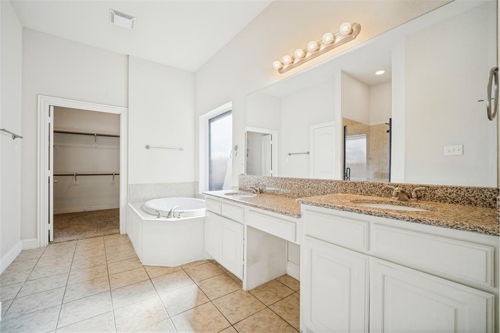 Dual-vanity cabinet with stone-finish countertops, undermount sinks, full-width mirror, and drop-in soaking tub with tiled surround
