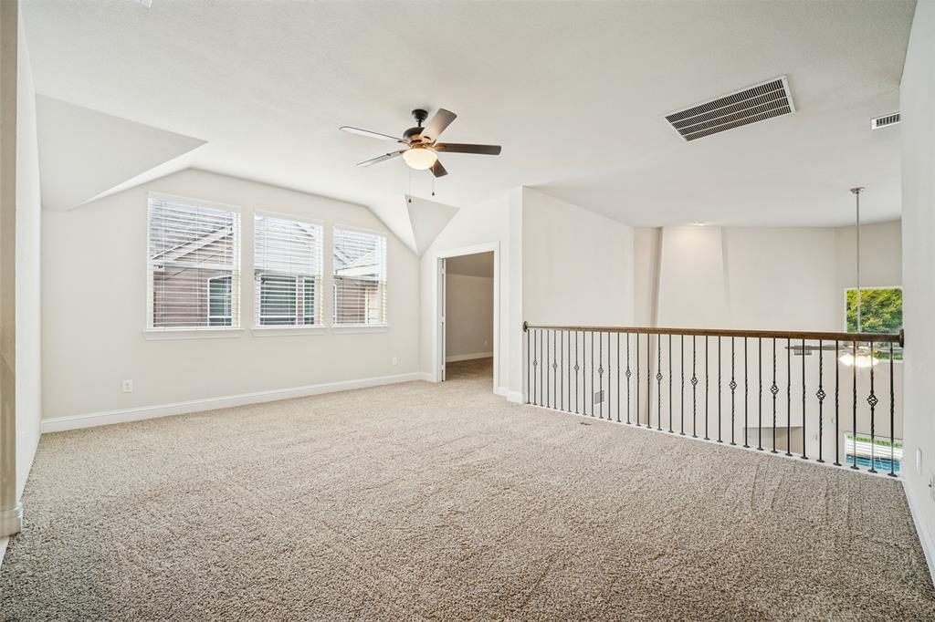 Open interior space featuring vaulted ceilings, a ceiling fan with integrated lighting, neutral wall-to-wall carpeting, and a wrought-iron baluster railing