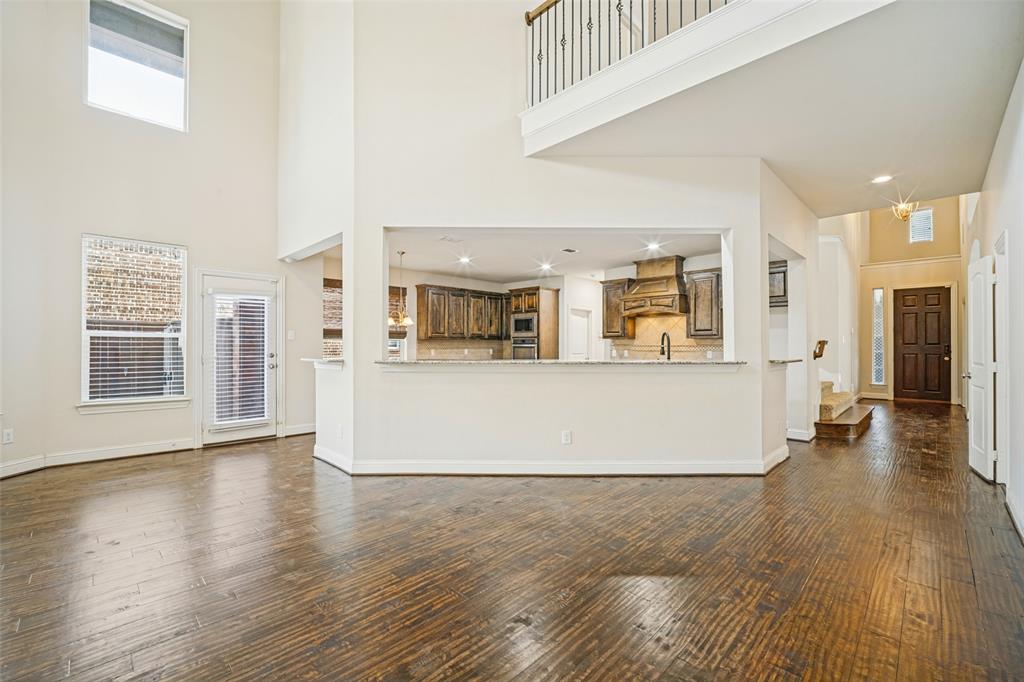 High-ceiling interior featuring wood-finish flooring, a kitchen pass-through with a stone-top breakfast bar, custom wood cabinetry, and a balcony with metal railing