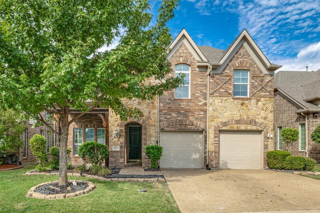 Two-story exterior featuring multi-textured brick and stone masonry, arched window detailing, double gabled roofline, and an attached two-car garage Two-story exterior featuring multi-textured brick and stone masonry, arched window detailing, double gabled roofline, and an attached two-car garage