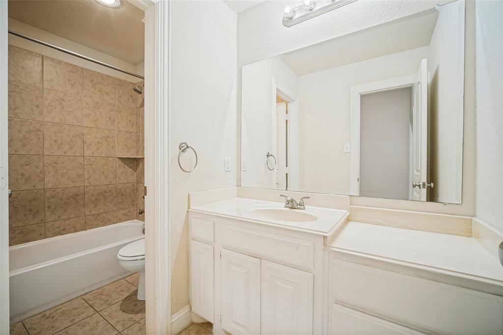Bathroom featuring a white vanity with an integrated countertop, large wall-mounted mirror, three-light fixture, and a tile-surround shower and tub combination