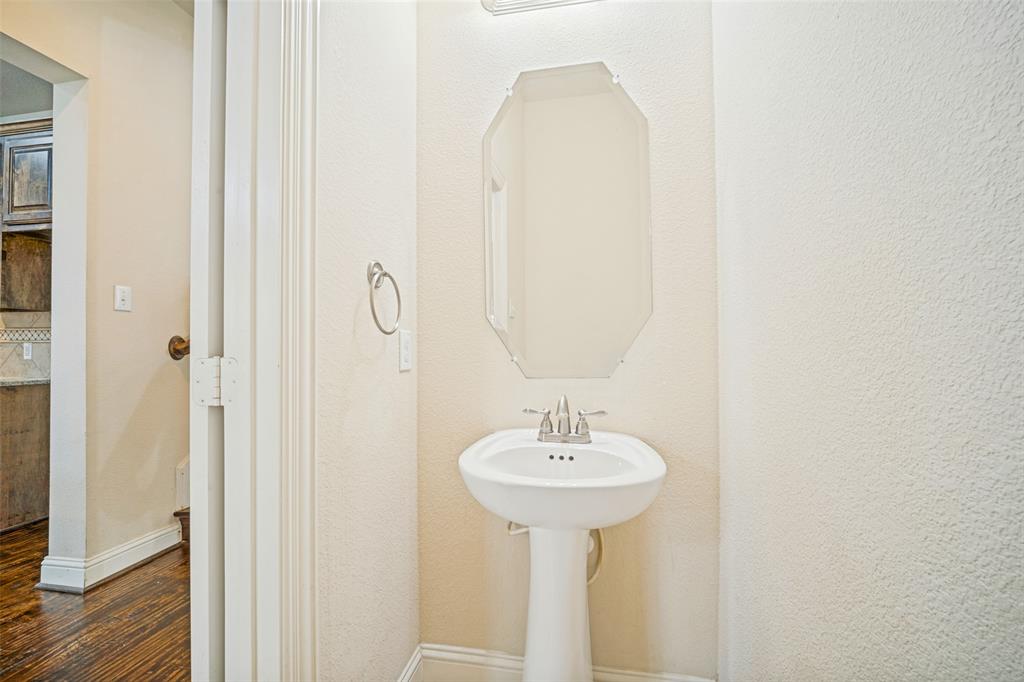 White porcelain pedestal sink, polished chrome widespread faucet, octagonal wall-mounted mirror, and wood-finish flooring
