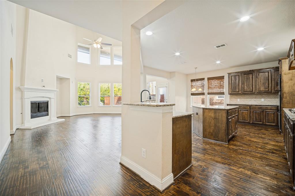 High-ceiling interior featuring dark-stained wood cabinetry, stone-finish countertops, wood-finish flooring, and a fireplace with a decorative mantel High-ceiling interior featuring dark-stained wood cabinetry, stone-finish countertops, wood-finish flooring, and a fireplace with a decorative mantel