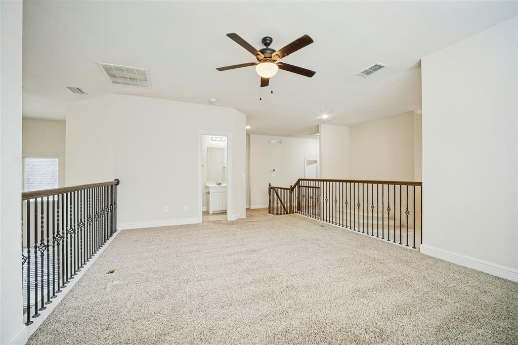Open-concept area featuring neutral wall tones, carpeted flooring, a ceiling fan with integrated lighting, and decorative metal baluster railings