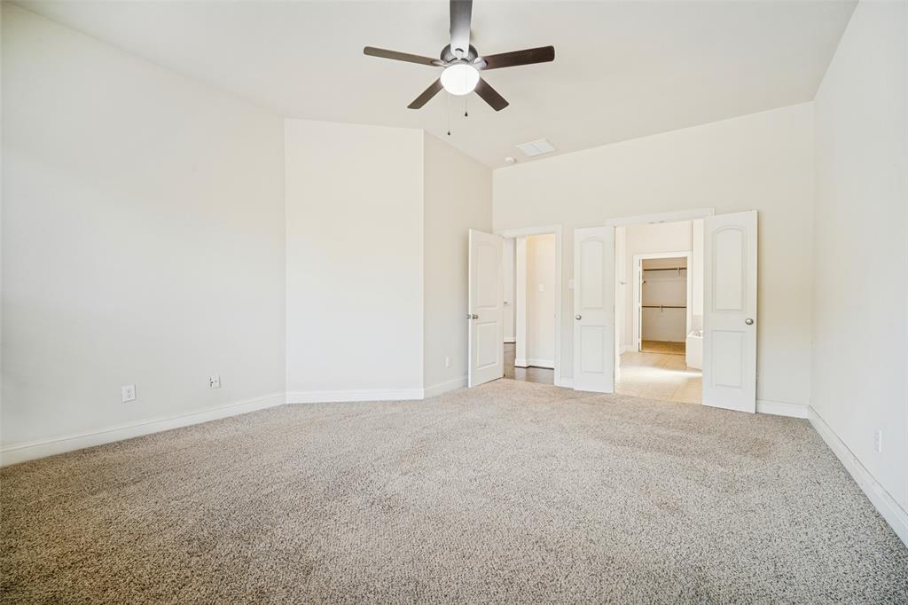 Spacious room featuring high ceilings, neutral wall color, carpeting, a ceiling fan with integrated lighting, and dual doors