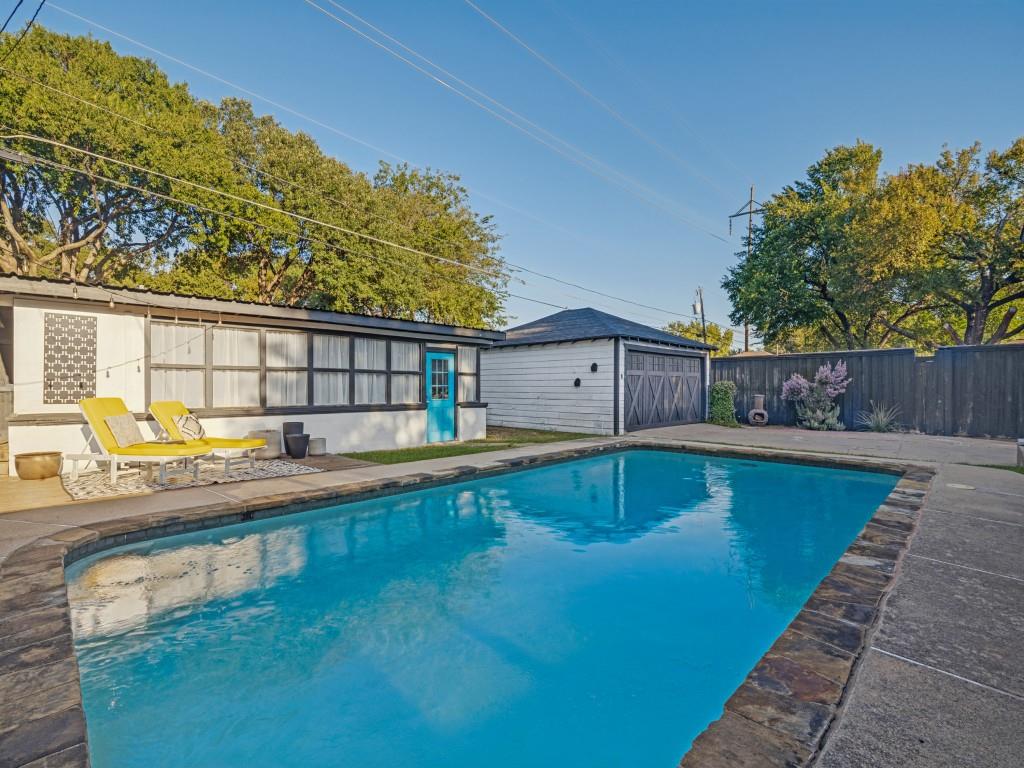 In-ground swimming pool with stone coping, concrete patio, detached garage, and wood privacy fencing