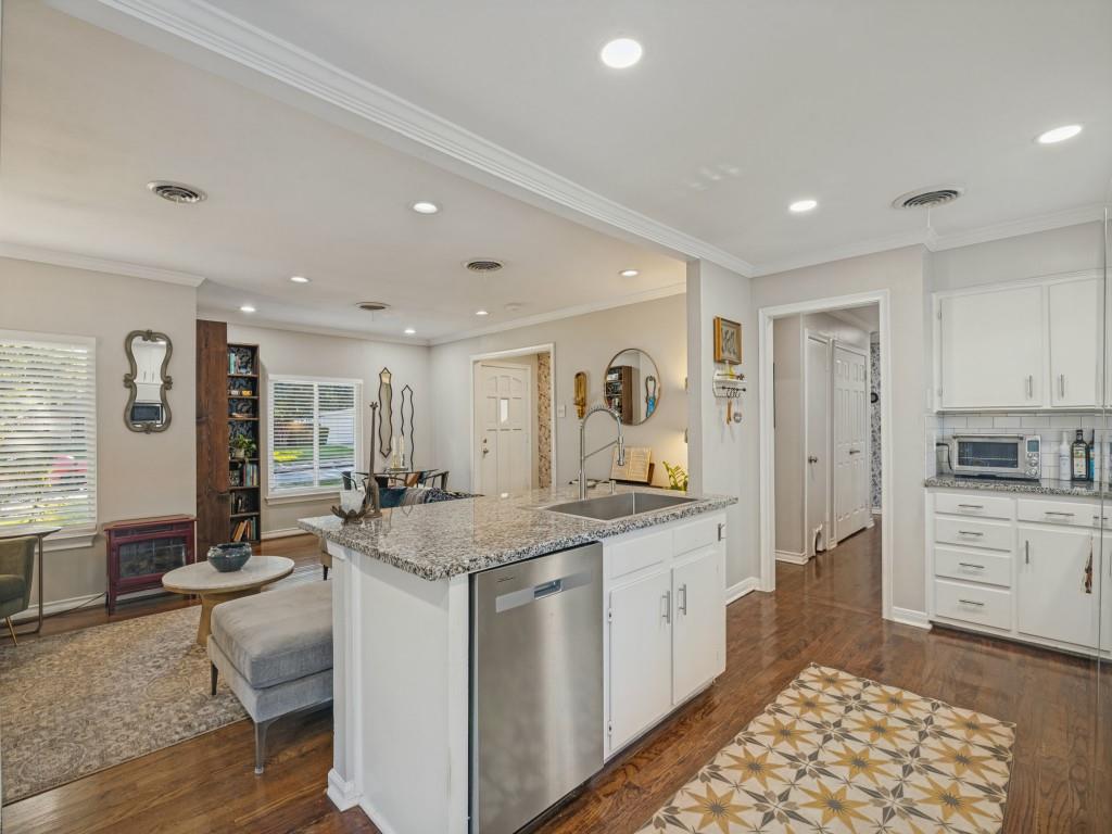 Kitchen featuring an island with a stone countertop, an integrated stainless steel dishwasher, white shaker-style cabinetry, recessed lighting, and wood-finish flooring