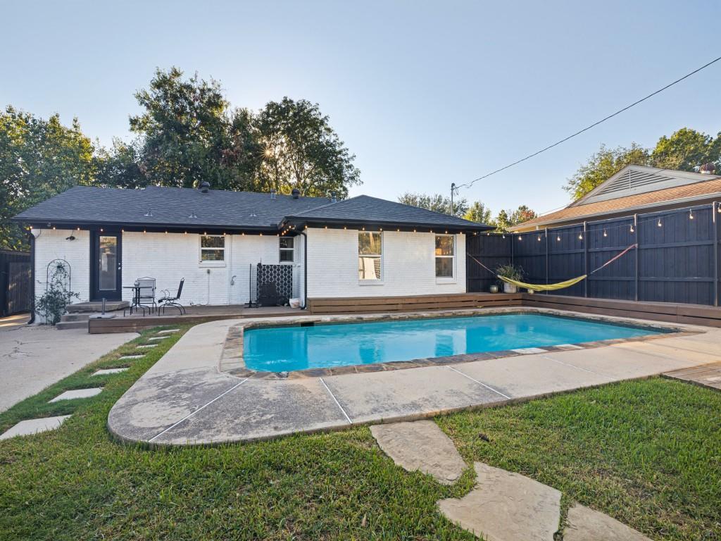 Backyard oasis featuring an in-ground pool, concrete decking, wood-plank perimeter fencing, and flagstone stepping stones set in the lawn
