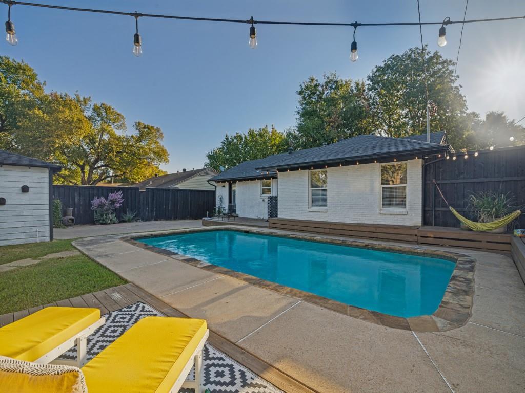 In-ground swimming pool with stone coping, white painted brick exterior, stained wood decking, and dark wood privacy fencing