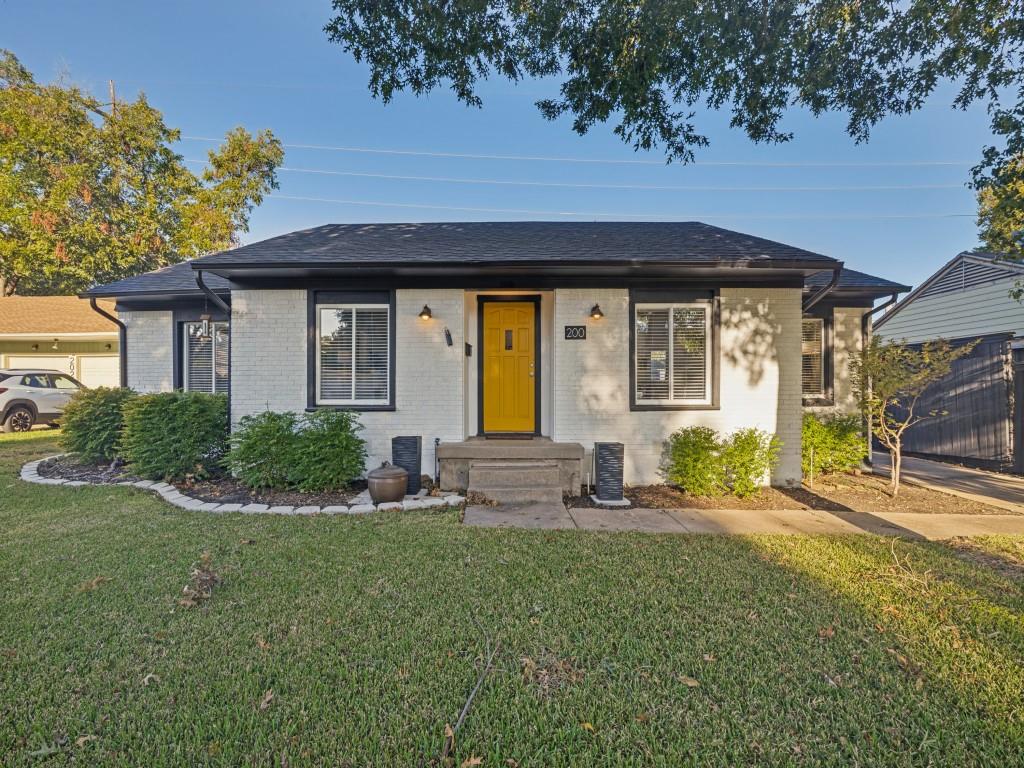 Single-story exterior featuring a painted brick facade, hip roof, contrasting window trim, concrete front steps, and landscaped garden beds