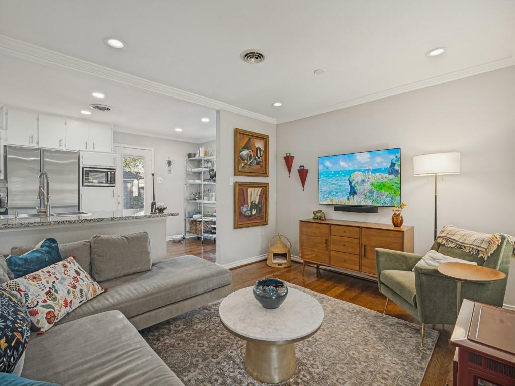 Open-concept interior featuring wood-finish flooring, recessed lighting, crown molding, and a kitchen peninsula with stone-finish countertops