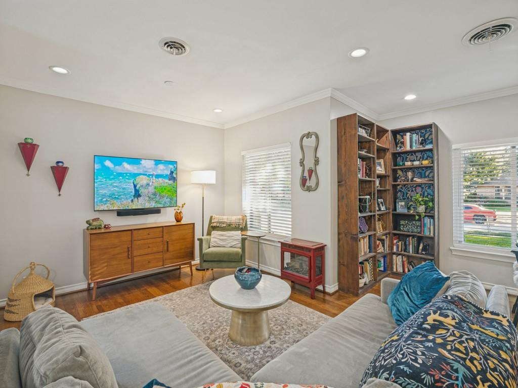 Living area featuring wood-finish flooring, recessed lighting, built-in floor-to-ceiling shelving, and windows equipped with horizontal blinds