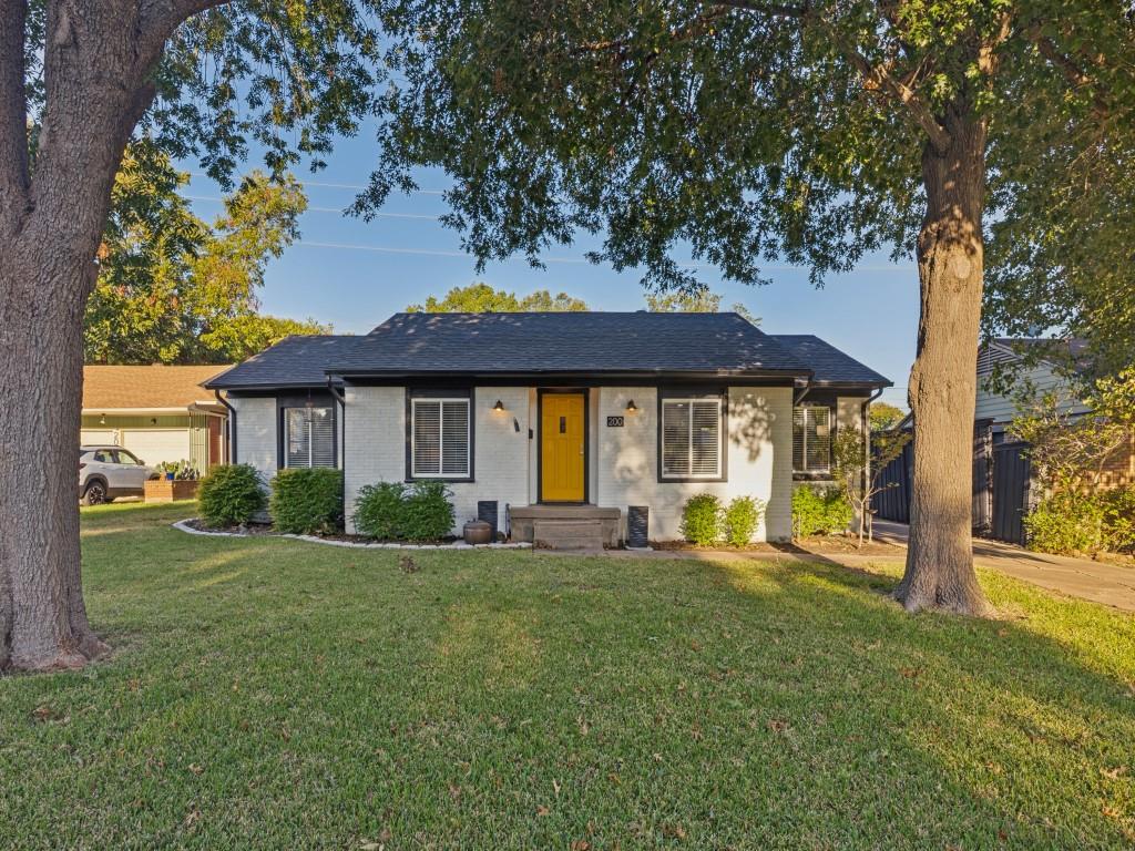 Single-story residence featuring a painted masonry exterior, shingle roof, contrasting window trim, and a prominent yellow entry door, situated on a lot with mature shade trees