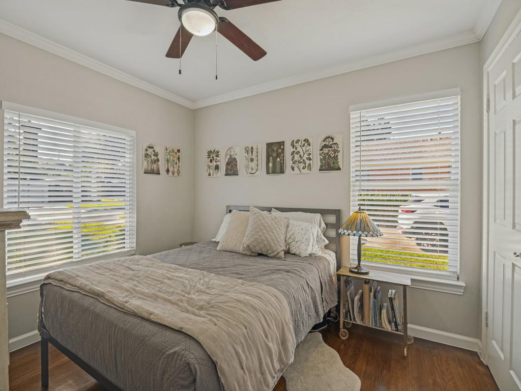 Neutral-toned walls, wood-finish flooring, crown molding, dual windows with horizontal blinds, and a ceiling fan with integrated light fixture