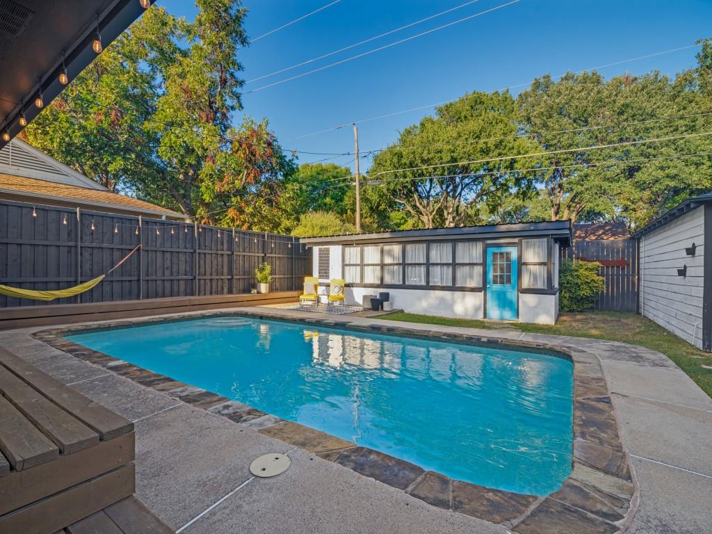 Outdoor area featuring an in-ground swimming pool, stone-trimmed concrete decking, a wood-surround pool deck, a detached structure with multi-pane windows, and a privacy fence
