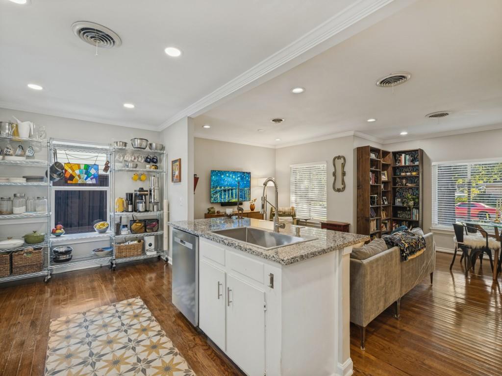 Kitchen island featuring a stone-look countertop, stainless steel undermount sink, and white cabinetry, complemented by wood-finish flooring and recessed lighting