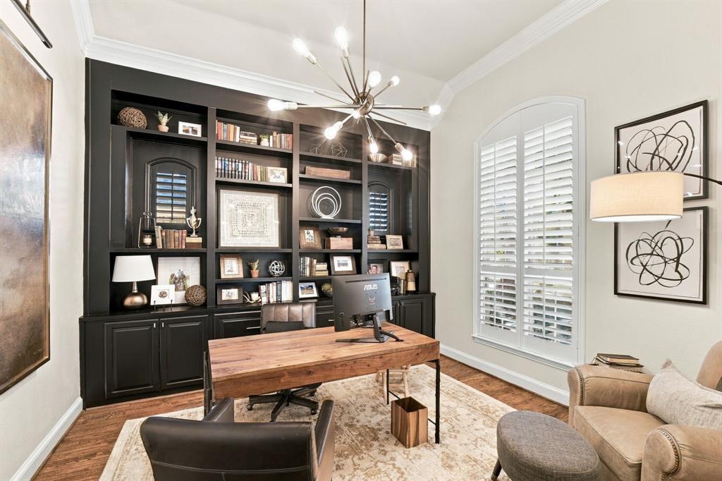 Custom floor-to-ceiling built-in cabinetry, arched window with plantation shutters, crown molding, and modern multi-arm chandelier