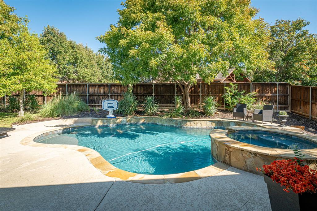 Freeform swimming pool with stone-tiled coping, integrated raised spa, concrete patio decking, and perimeter wood privacy fencing