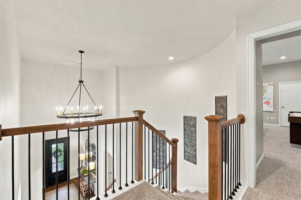 Curved wall design featuring a staircase with wood-finish railing, metal balusters, and a tiered chandelier