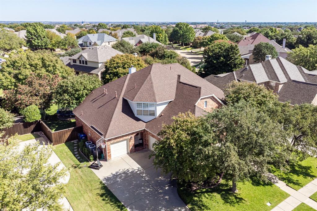 Aerial perspective of a multi-gabled roofline, brick exterior, concrete driveway, and mature landscaping