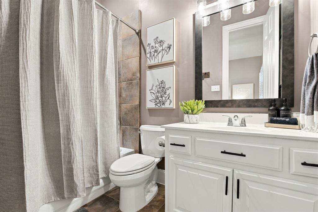 White vanity with rectangular basin and matte black hardware, framed wall-mounted mirror with integrated lighting, and stone-finish shower surround