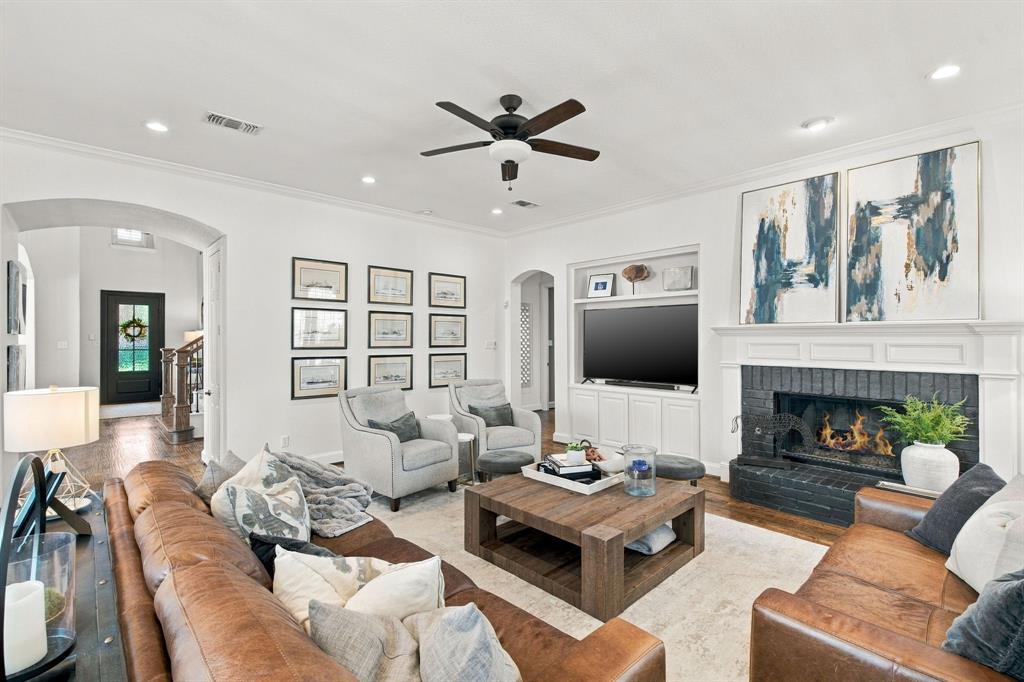 Living room featuring a dark-painted masonry fireplace with a white mantel, built-in cabinetry, arched architectural openings, recessed lighting, and a ceiling fan