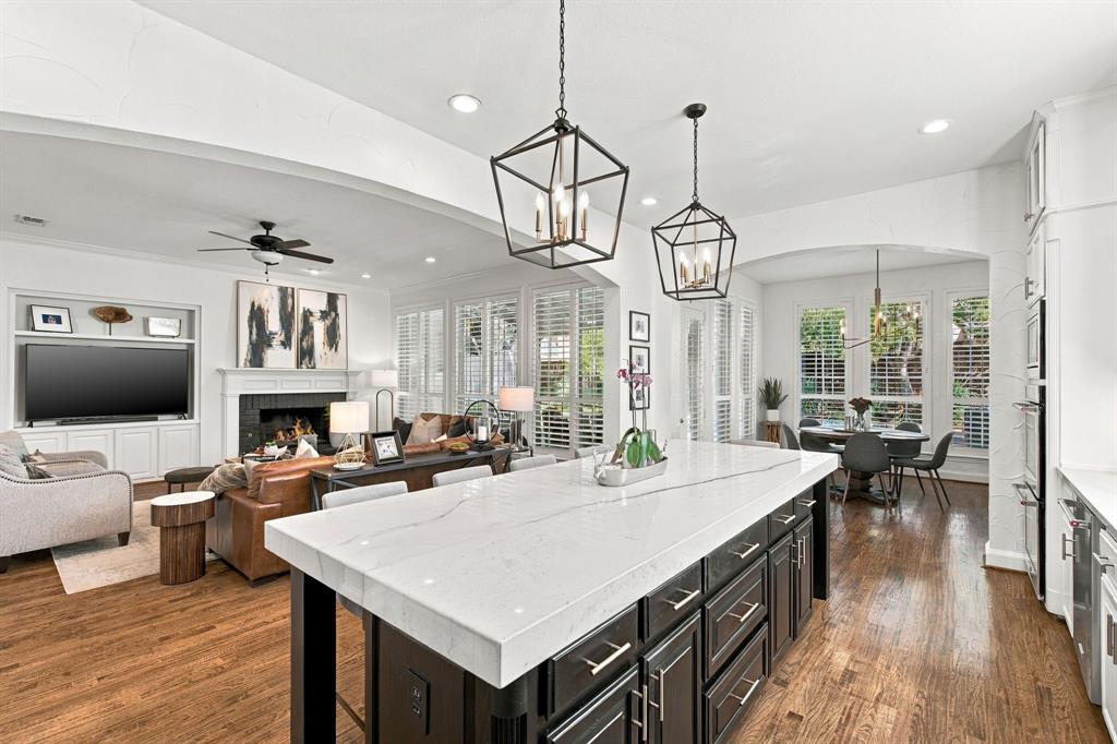 Kitchen island featuring a stone-look countertop and dark cabinetry, wood-finish flooring, geometric pendant lighting, and a built-in media center with a fireplace