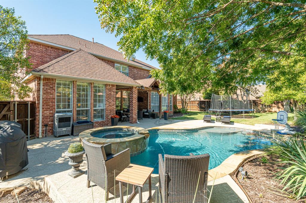 Red brick exterior featuring a multi-level roofline, swimming pool with a raised stone-accented spa, covered patio, and manicured lawn