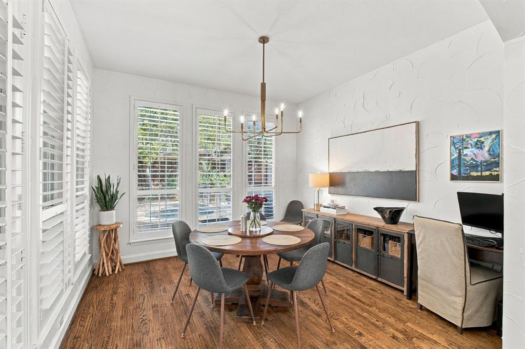 Dining area featuring wood-finish flooring, textured wall detailing, floor-to-ceiling windows with plantation shutters, and a multi-arm metallic chandelier