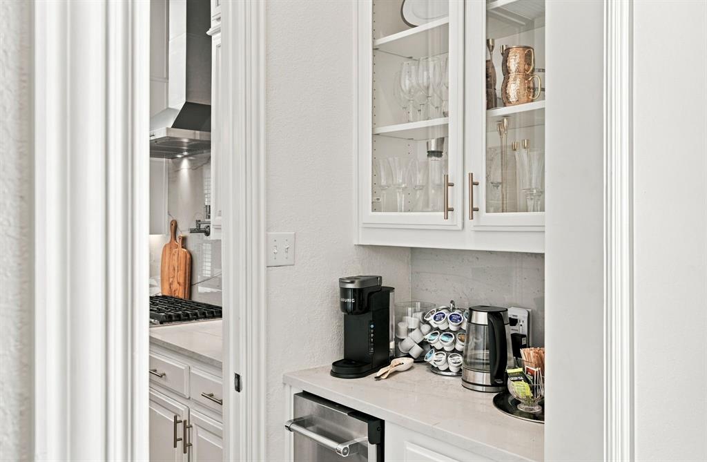 White cabinetry with glass-panel upper doors, stone-finish countertops, stainless steel under-counter appliance, and stone-tiled backsplash