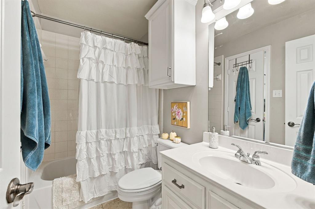Bathroom featuring a white vanity with an integrated sink, polished chrome faucet, wall-mounted storage cabinet, full-width mirror with overhead light fixture, and a tile-surround bathtub