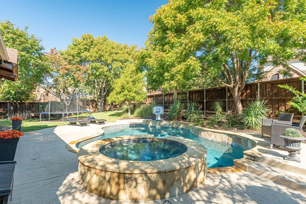 Custom in-ground swimming pool with an integrated elevated spa, natural stone coping, concrete patio, and perimeter wood privacy fencing