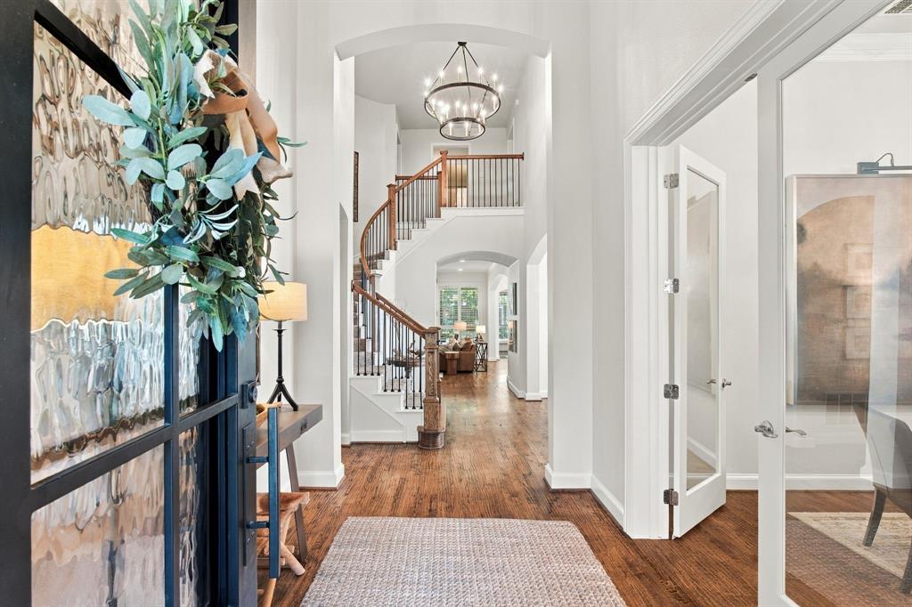 Entryway featuring wood-finish flooring, a curved staircase with a wooden banister, arched openings, a multi-tiered metal chandelier, and a glass-paneled entry door