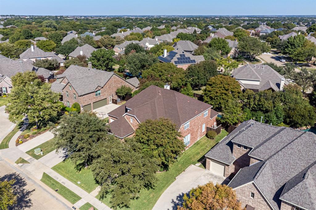 Aerial perspective of a brick-exterior residence featuring a multi-gabled roofline, a concrete driveway, and mature landscaping