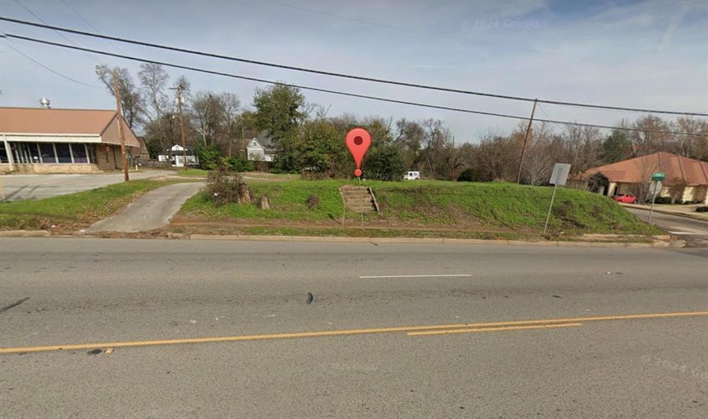 Vacant lot featuring a paved driveway, elevated grass terrain, and concrete steps