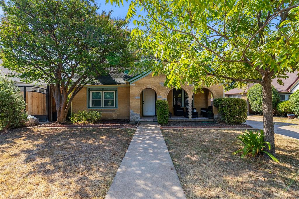 Brick exterior with arched entryway, covered front porch, and mature trees