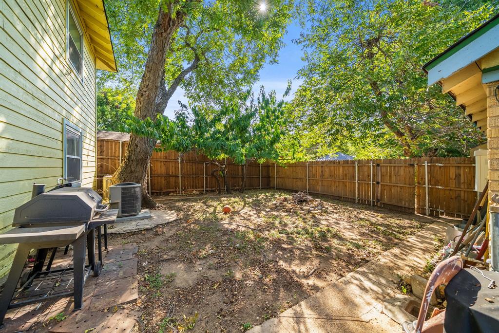 Expansive backyard featuring a wood fence, mature trees, and a concrete patio