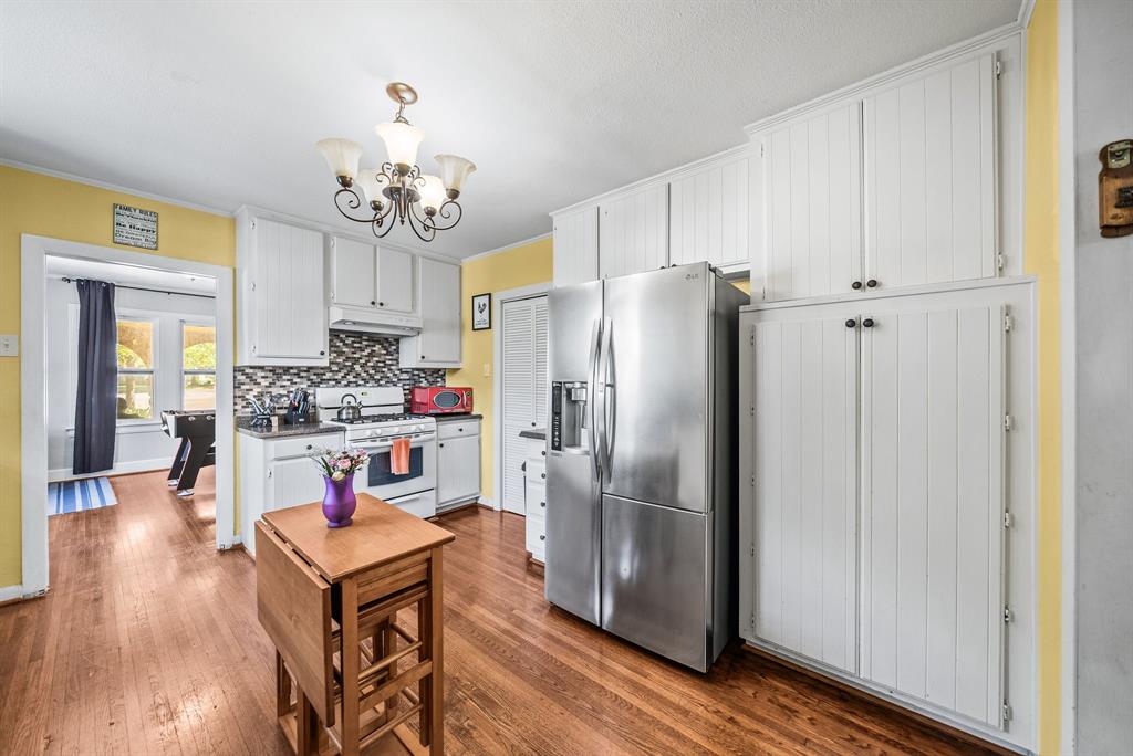 Kitchen featuring wood-finish flooring, white cabinetry, a mosaic tile backsplash, and a stainless steel refrigerator