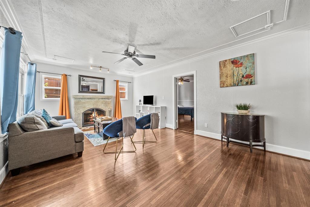 Hardwood flooring, fireplace with stone surround, ceiling fan, crown molding, and white baseboards