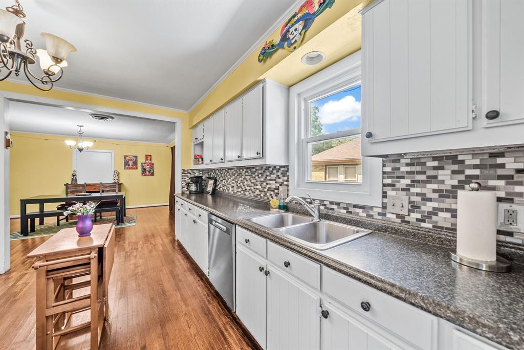 Kitchen featuring white cabinetry, dark speckled countertops, a mosaic tile backsplash, stainless steel sink, and wood-finish flooring