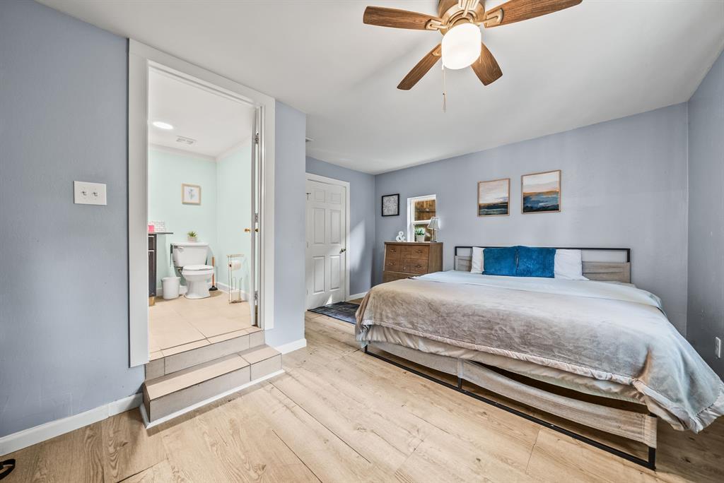 Wood-finish flooring throughout, ceiling fan with integrated lighting, and a private attached bathroom featuring tile flooring