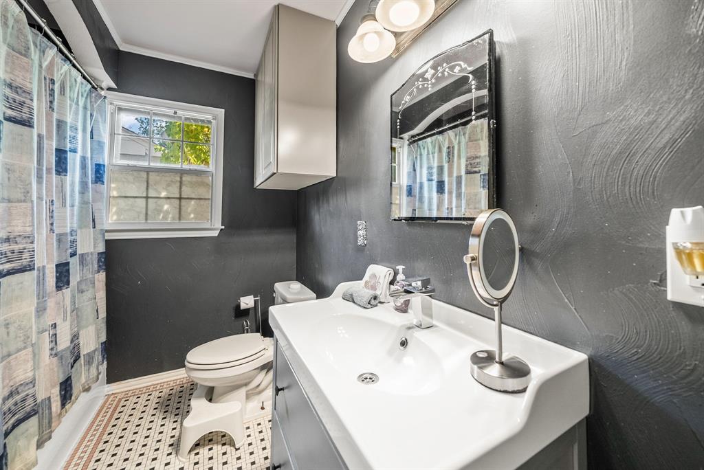 Bathroom featuring a single vanity with integrated sink, wall-mounted cabinetry, a window with privacy glass, and patterned floor tiling