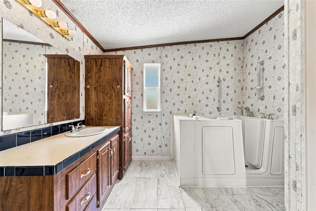 Bathroom featuring a walk-in tub with integrated safety bars, wood-finish cabinetry, a large wall-mounted mirror, and tile flooring