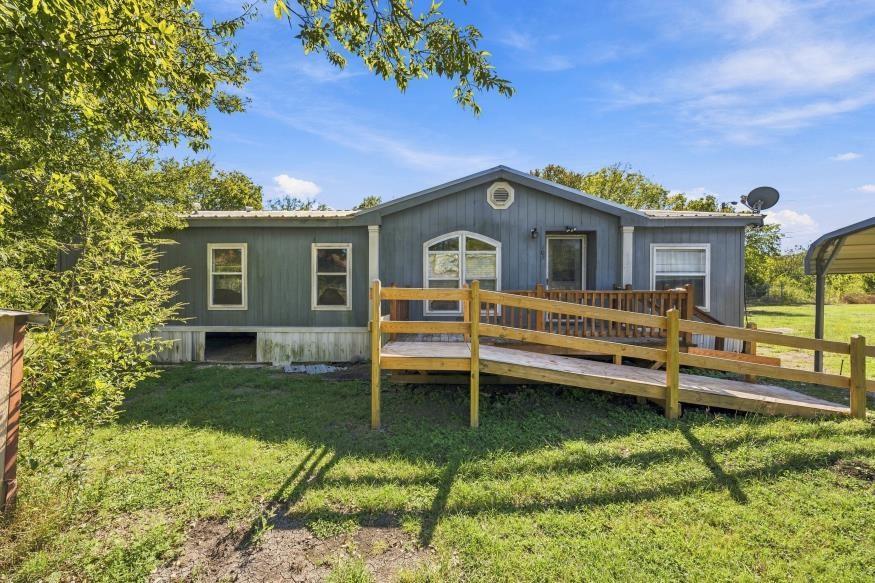 Single-story residence featuring wood-tone exterior siding, a gable roofline, an arched window, and a wooden accessibility ramp leading to the entryway